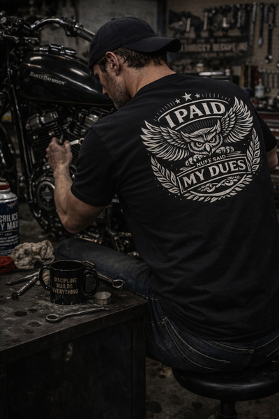 Person working on a motorcycle in a workshop with 'Paid My Dues' shirt.